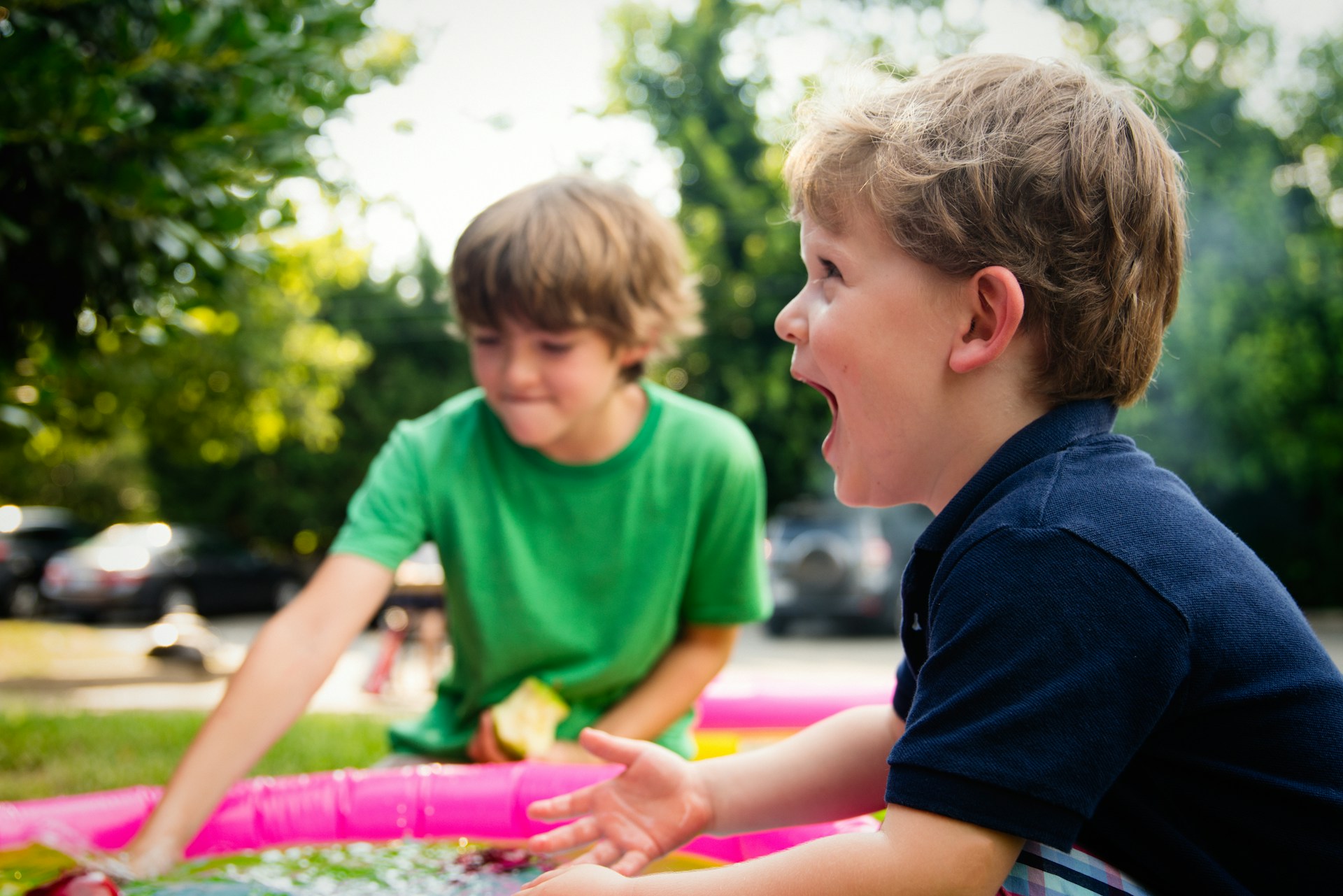 Two boys talking beside a paddling pool in a backyard